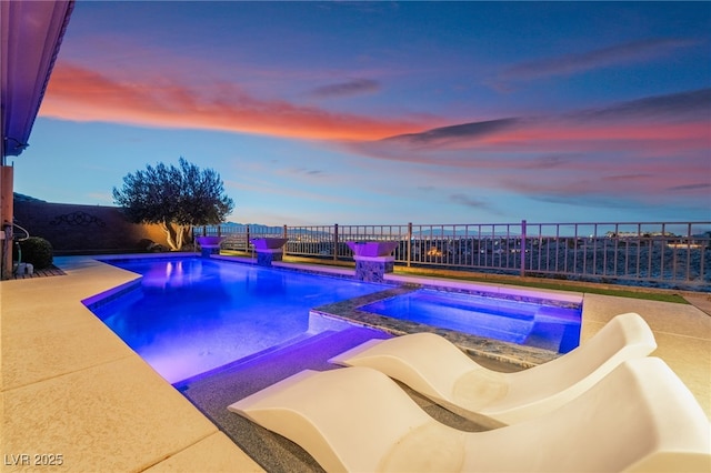 pool at dusk with an in ground hot tub and a patio