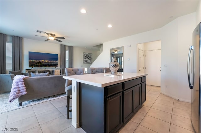 kitchen featuring ceiling fan, a center island, stainless steel refrigerator, a kitchen breakfast bar, and light tile patterned floors