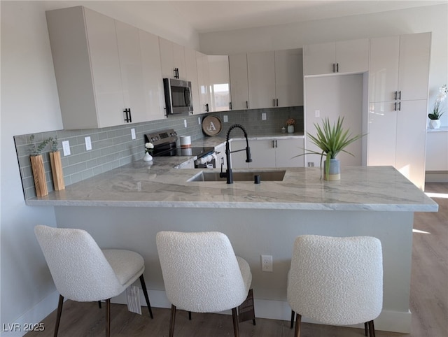 kitchen featuring white cabinetry, appliances with stainless steel finishes, kitchen peninsula, and sink