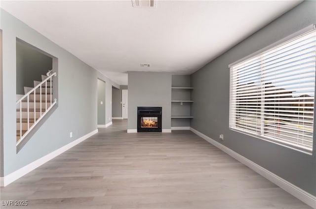 unfurnished living room featuring a multi sided fireplace and light hardwood / wood-style floors