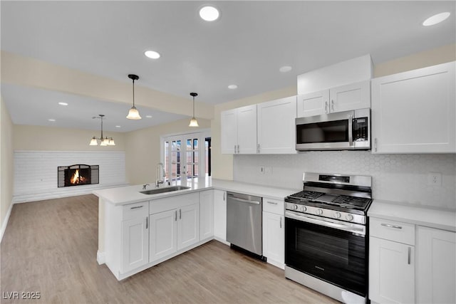 kitchen with sink, white cabinetry, decorative light fixtures, appliances with stainless steel finishes, and kitchen peninsula