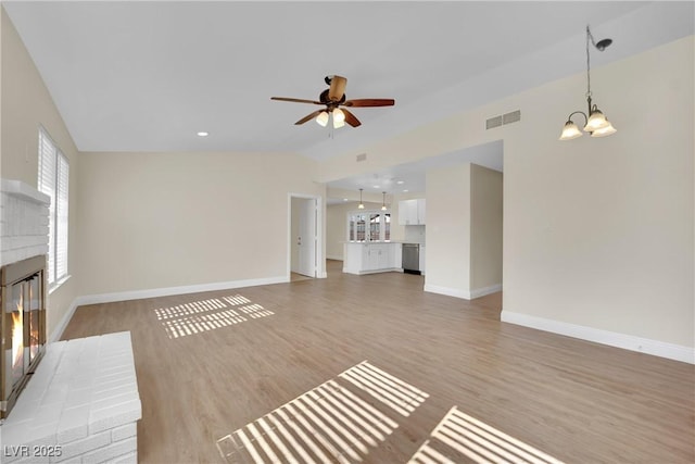 unfurnished living room with lofted ceiling, ceiling fan with notable chandelier, a brick fireplace, and light wood-type flooring