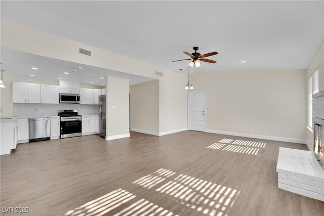 unfurnished living room with a brick fireplace, light hardwood / wood-style flooring, sink, and ceiling fan