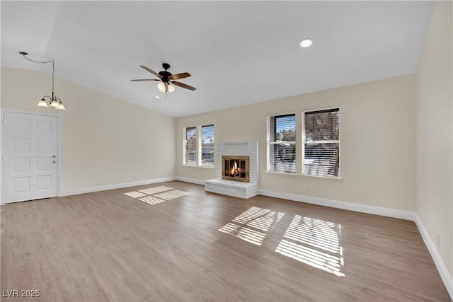 unfurnished living room featuring vaulted ceiling, wood-type flooring, a brick fireplace, and ceiling fan with notable chandelier