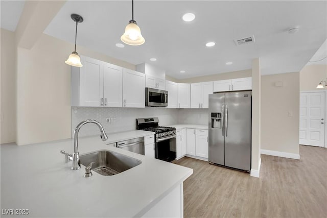 kitchen featuring white cabinetry, sink, hanging light fixtures, stainless steel appliances, and light hardwood / wood-style flooring