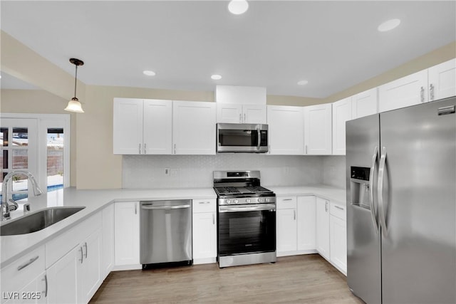 kitchen featuring pendant lighting, sink, white cabinets, light hardwood / wood-style floors, and stainless steel appliances