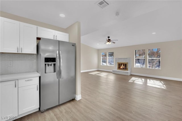 kitchen featuring a brick fireplace, ceiling fan, white cabinets, and stainless steel refrigerator with ice dispenser