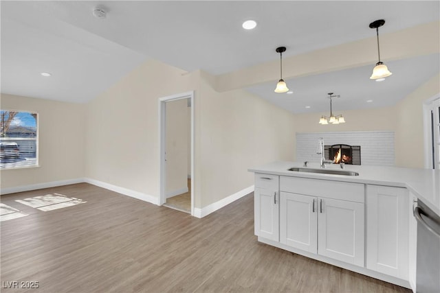 kitchen with sink, white cabinetry, hanging light fixtures, stainless steel dishwasher, and light wood-type flooring