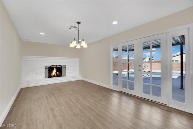 unfurnished living room with an inviting chandelier, hardwood / wood-style floors, a fireplace, and french doors