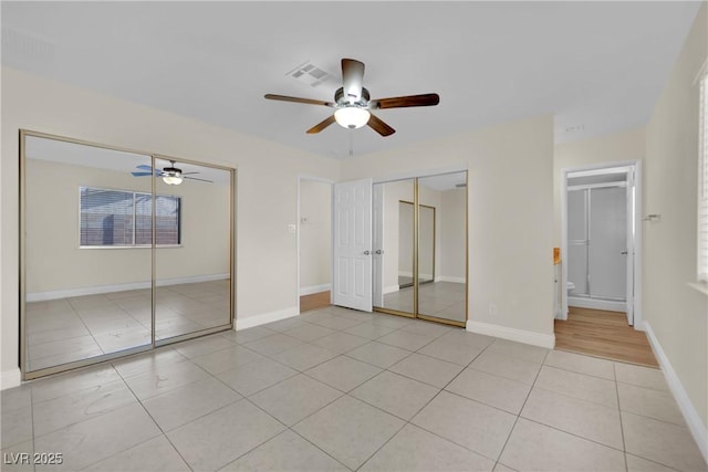 unfurnished bedroom with multiple closets, ceiling fan, connected bathroom, and light tile patterned floors