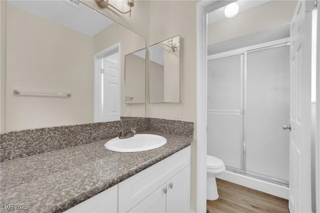 bathroom with a shower with door, vanity, wood-type flooring, and toilet