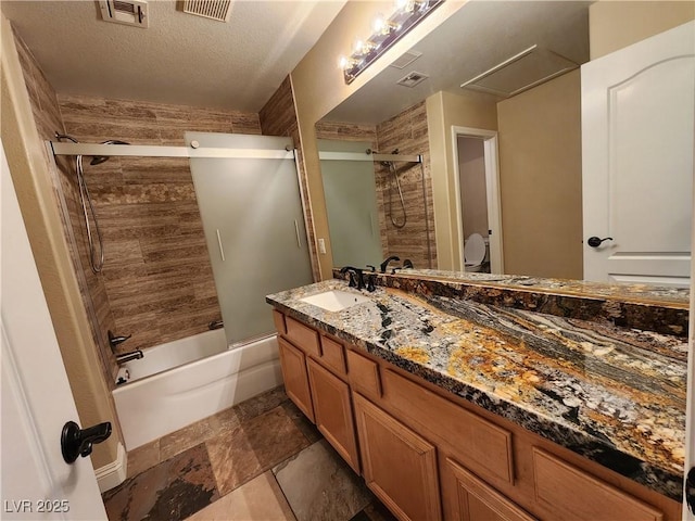 full bathroom featuring a textured ceiling, toilet, vanity, and shower / bath combination with glass door