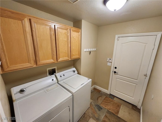 washroom featuring a textured ceiling, washing machine and clothes dryer, and cabinets