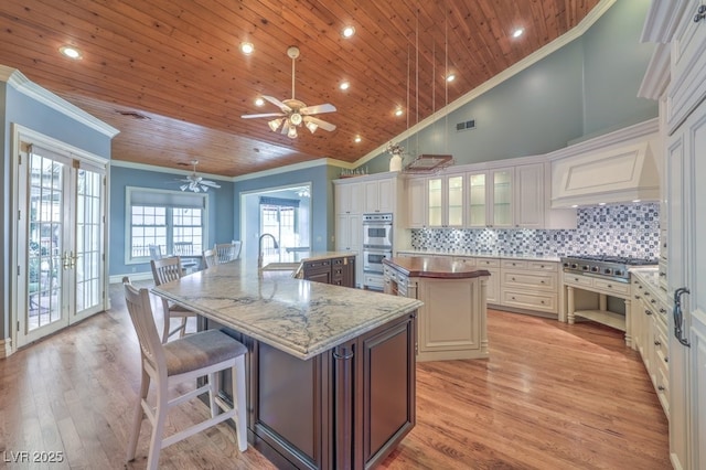 kitchen with appliances with stainless steel finishes, decorative backsplash, french doors, a large island with sink, and light stone counters