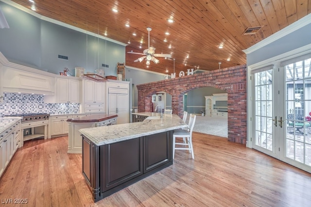 kitchen featuring backsplash, a spacious island, a towering ceiling, french doors, and dark stone counters