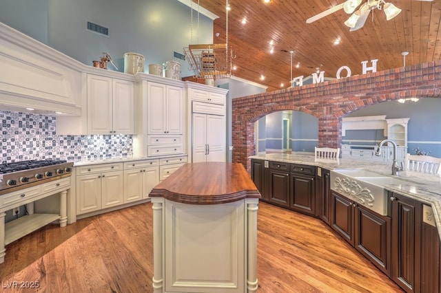 kitchen with butcher block countertops, wooden ceiling, decorative backsplash, a spacious island, and sink