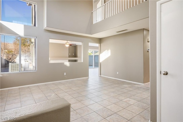 empty room featuring ceiling fan, a high ceiling, and light tile patterned floors