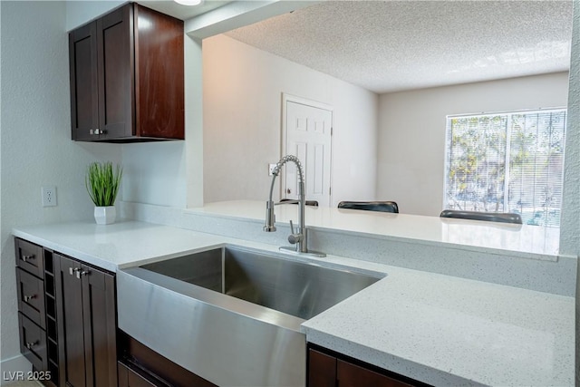 kitchen with light stone counters, sink, a textured ceiling, and dark brown cabinets