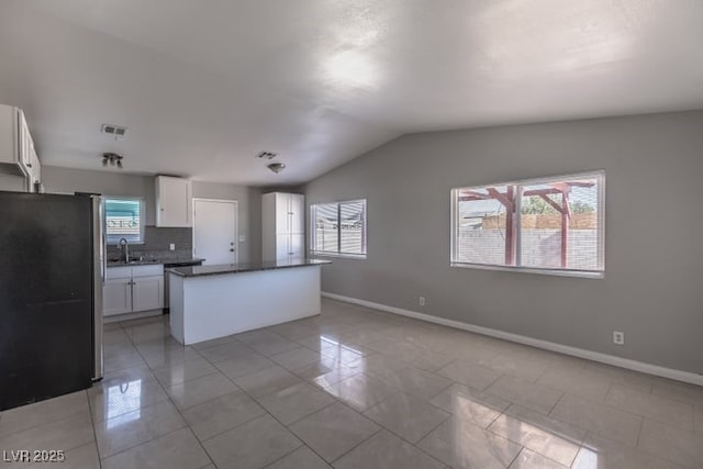 kitchen featuring plenty of natural light, stainless steel fridge, white cabinets, and vaulted ceiling