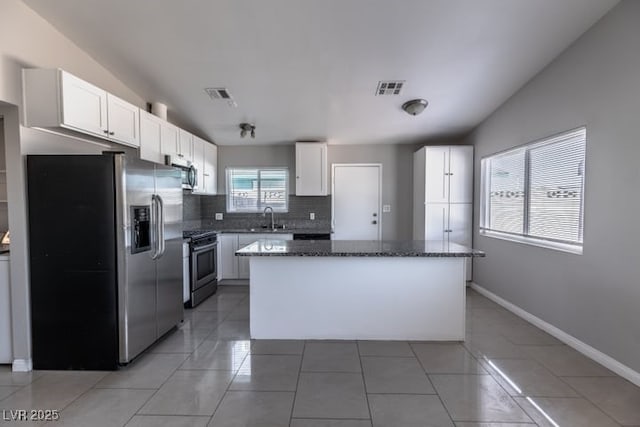 kitchen with appliances with stainless steel finishes, dark stone countertops, white cabinetry, and a kitchen island