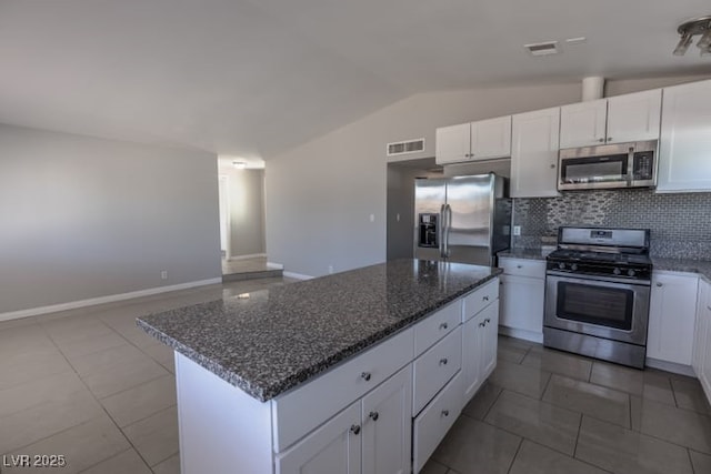 kitchen featuring appliances with stainless steel finishes, backsplash, dark stone countertops, vaulted ceiling, and white cabinets