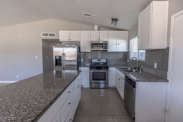 kitchen with vaulted ceiling, sink, appliances with stainless steel finishes, white cabinets, and dark stone counters