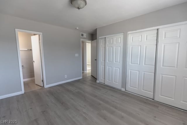 unfurnished bedroom featuring multiple closets, connected bathroom, and light hardwood / wood-style flooring