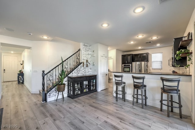 kitchen with kitchen peninsula, stainless steel appliances, a breakfast bar area, and light wood-type flooring