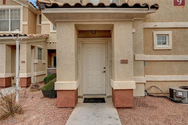 entrance to property featuring a tiled roof, central AC unit, and stucco siding