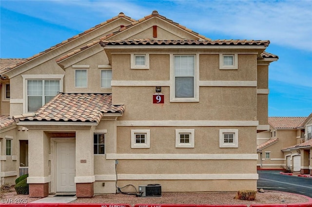 view of front facade with a tiled roof, central AC unit, and stucco siding