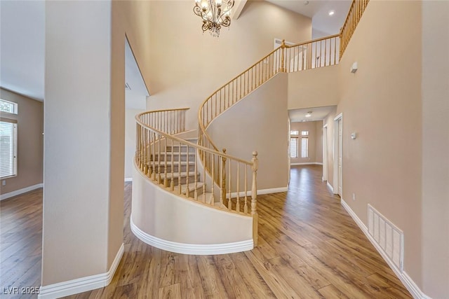 stairway with a towering ceiling, a notable chandelier, and hardwood / wood-style floors