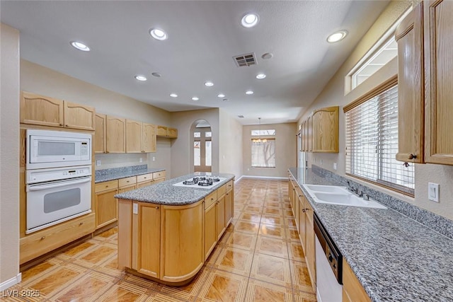 kitchen with a center island, sink, white appliances, light tile patterned floors, and light brown cabinetry