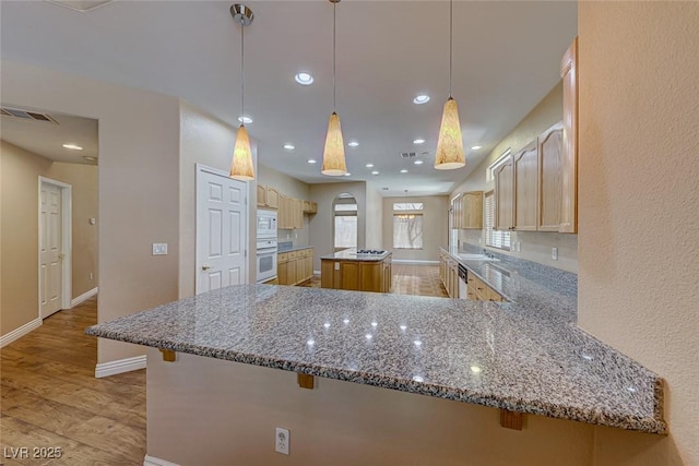 kitchen with white appliances, light brown cabinets, hanging light fixtures, kitchen peninsula, and stone counters