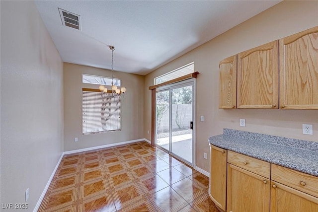 kitchen with light stone countertops, light brown cabinets, a chandelier, and pendant lighting