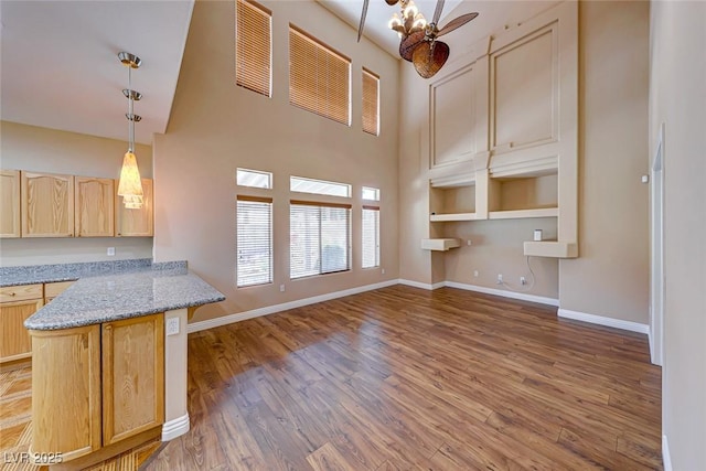 kitchen featuring ceiling fan, light brown cabinets, light stone counters, and decorative light fixtures