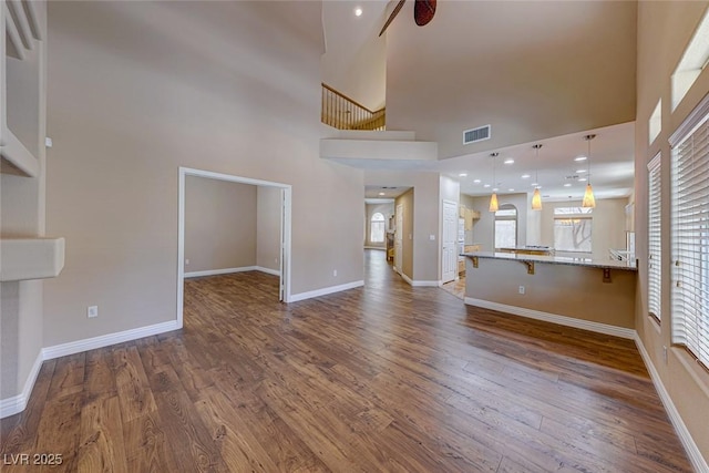 unfurnished living room with ceiling fan, a high ceiling, and hardwood / wood-style floors