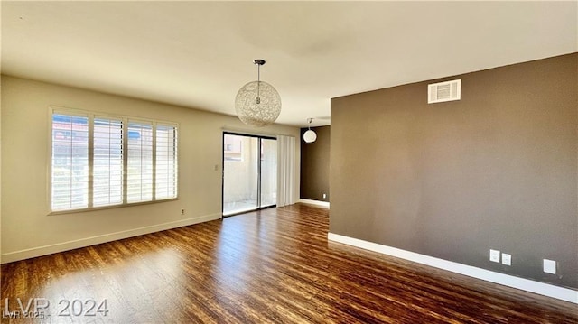 empty room with dark hardwood / wood-style floors and an inviting chandelier