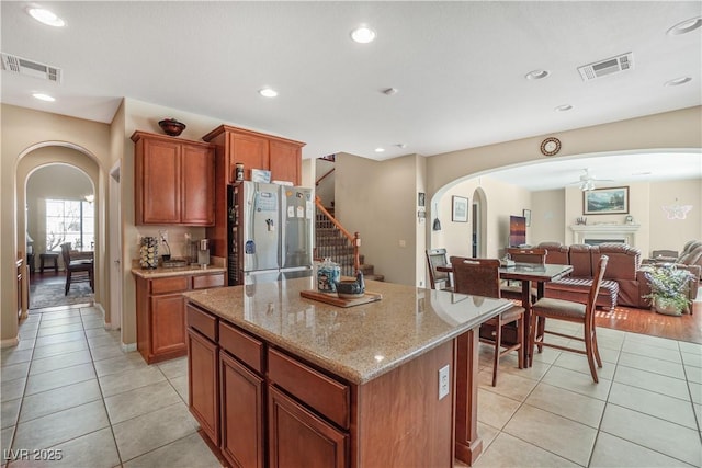 kitchen with light stone countertops, a center island, stainless steel refrigerator, ceiling fan, and light tile patterned floors