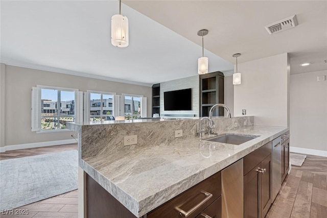 kitchen featuring pendant lighting, stainless steel dishwasher, sink, light wood-type flooring, and light stone countertops