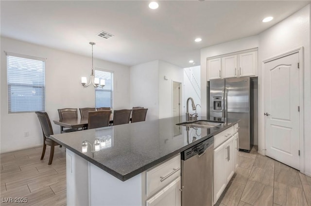 kitchen featuring a center island with sink, sink, hanging light fixtures, stainless steel appliances, and white cabinets