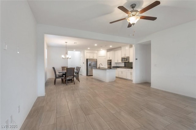 kitchen with appliances with stainless steel finishes, hanging light fixtures, ceiling fan with notable chandelier, white cabinets, and sink