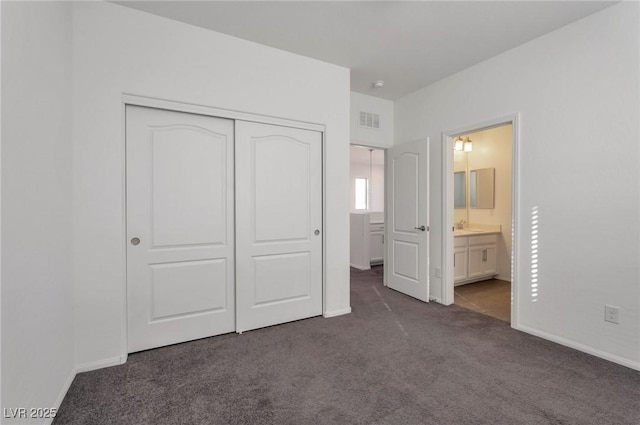 unfurnished bedroom featuring ensuite bath, a closet, sink, and dark colored carpet