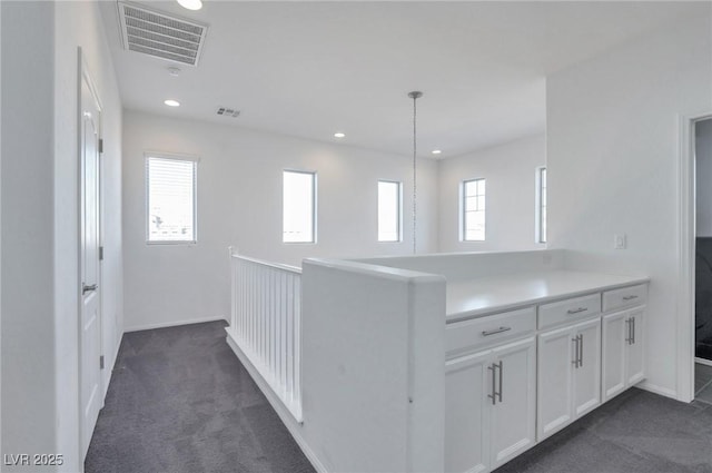 interior space with decorative light fixtures, dark carpet, white cabinets, and kitchen peninsula