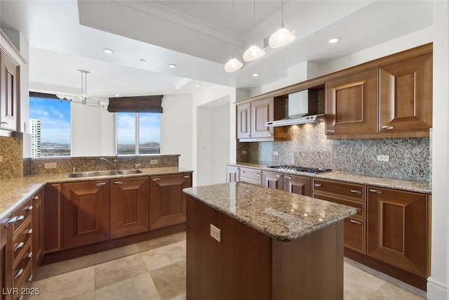 kitchen with stainless steel gas stovetop, a center island, decorative light fixtures, wall chimney exhaust hood, and sink