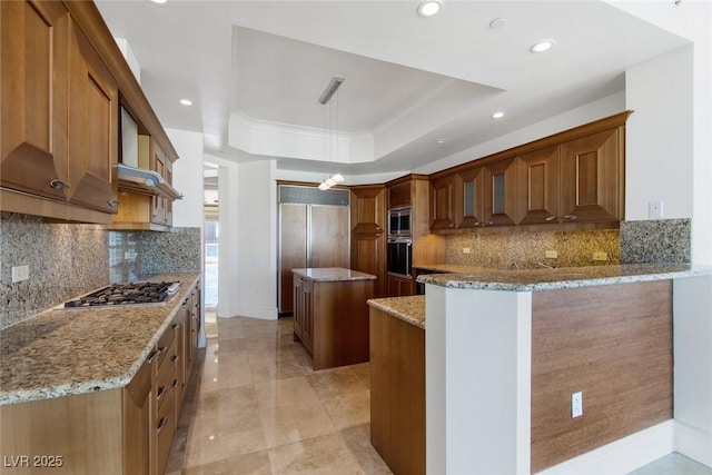 kitchen with a kitchen island, built in appliances, backsplash, light stone counters, and a tray ceiling