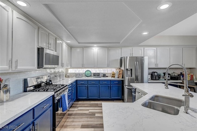 kitchen featuring light stone counters, blue cabinetry, appliances with stainless steel finishes, and a raised ceiling