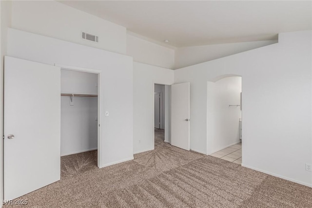 unfurnished bedroom with light carpet, a closet, a walk in closet, and lofted ceiling