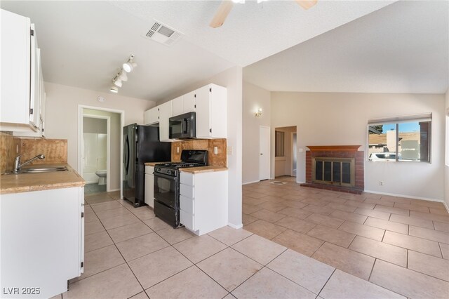 kitchen with black appliances, lofted ceiling, white cabinetry, sink, and a brick fireplace