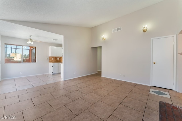 tiled empty room featuring lofted ceiling, a textured ceiling, and ceiling fan