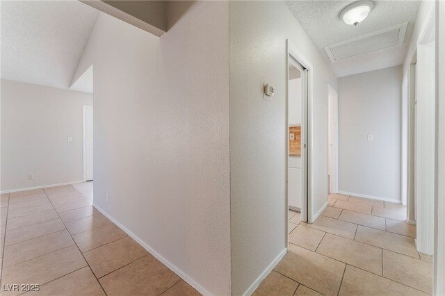 hall featuring light tile patterned flooring, vaulted ceiling, and a textured ceiling